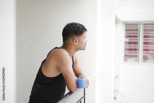 Portrait of a handsome Indian Bengali brunette man wearing a black western inner looking thoughtfully standing on a balcony. Indian lifestyle and fashion portrait