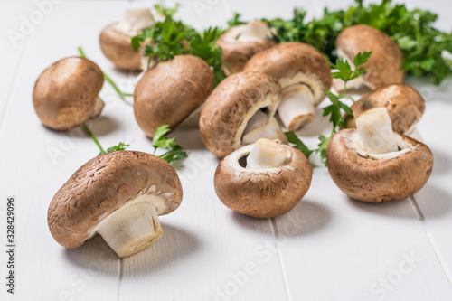 Parsley leaves and Royal mushrooms scattered on a white wooden table. Vegetarian food.
