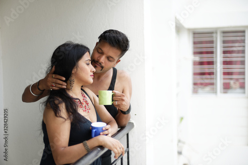Indian Bengali beautiful brunette couple in black dress sharing intimate romantic moments while drinking tea/coffee standing on balcony in white background. Indian lifestyle  and romantic couple