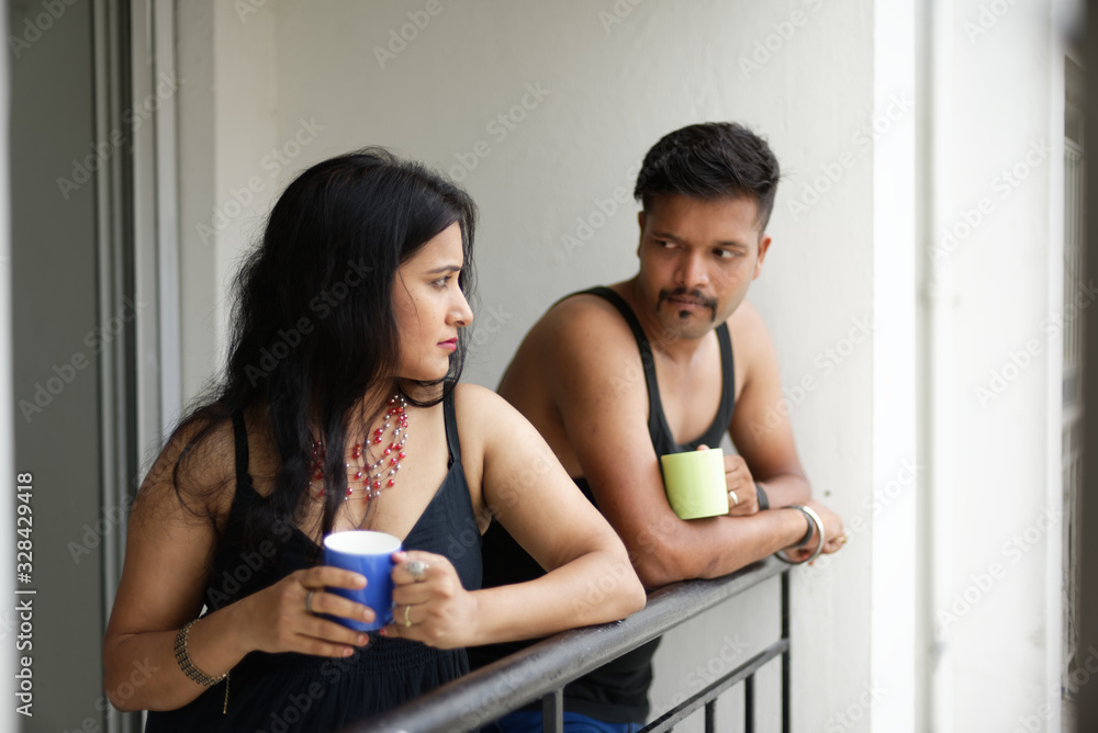 Indian Bengali beautiful brunette sad and depressed couple drinking tea/coffee standing on balcony in white background. Indian lifestyle  and depressed couple