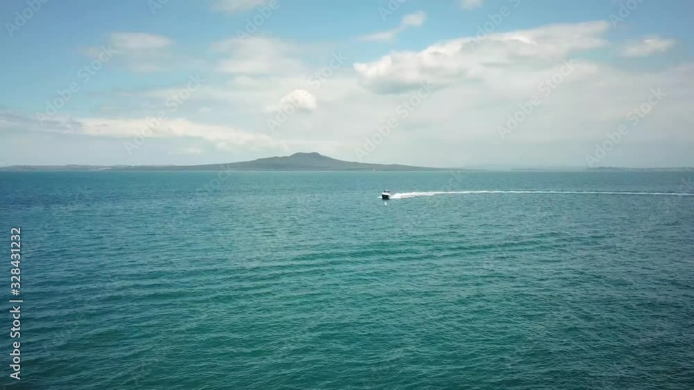 Aerial drone shot, of a fast boat travelling towards the camera with Rangitoto Island as background in New Zealand. Aerial drone shot, of a fast boat travelling towards the camera with Rangitoto Island as background in New Zealand.
