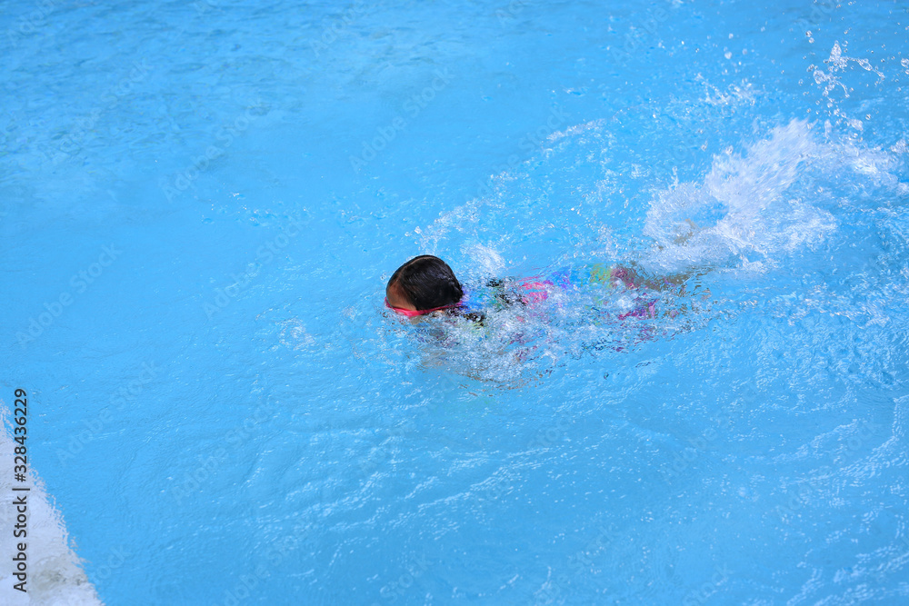 Asian little child girl learning to swim in pool. Schoolgirl practicing to swimming.