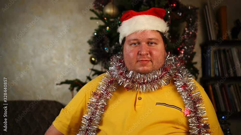 Man in Santa hat and tinsel looking at camera and saying yes by shaking his head Man in Santa hat and tinsel looking at camera and saying yes by shaking his head