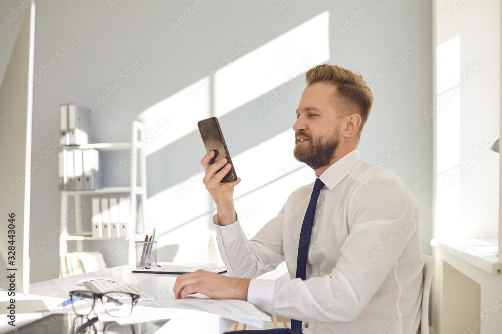 Serious busy businessman reads message on the phone at a table with a computer in the office. Serious busy businessman reads message on the phone at a table with a computer in the office.