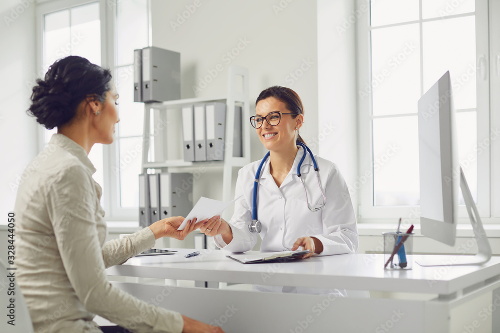 © Studio Romantic - Smiling female patient at consultation with woman doctor sitting at table in office clinic.