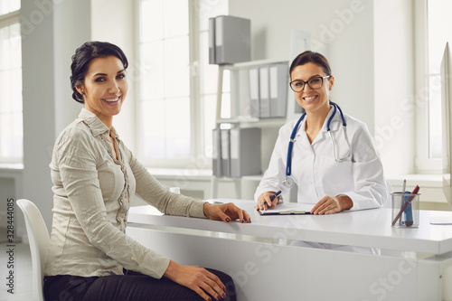 Smiling female patient at consultation with woman doctor sitting at table in office clinic.