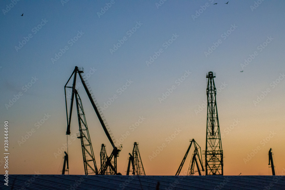 Cargo cranes silhouettes against dramatic blue and orange sunset sky, Varna, Bulgaria, crane in the port