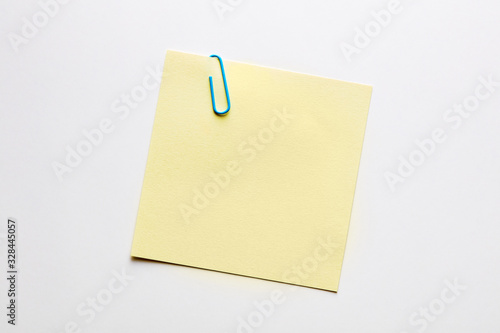 Blank yellow note paper or notepad with a blue paper clip on white background with copy space