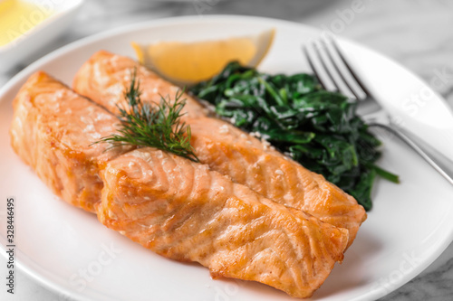 Tasty salmon with spinach and lemon on plate, closeup