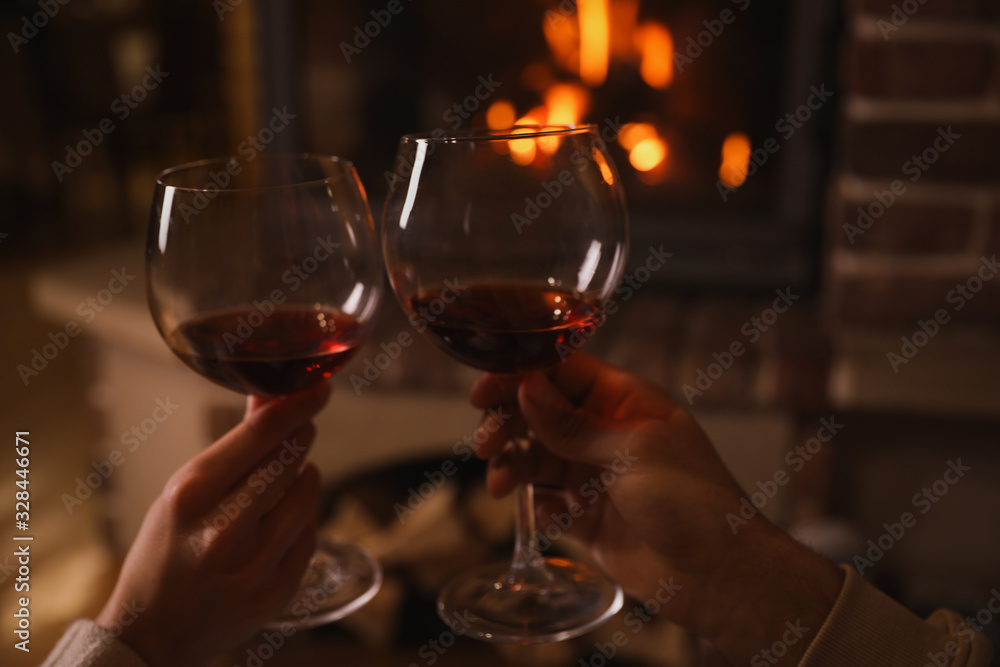 Couple with glasses of red wine near burning fireplace, closeup