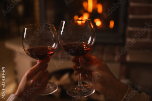 Couple with glasses of red wine near burning fireplace  closeup