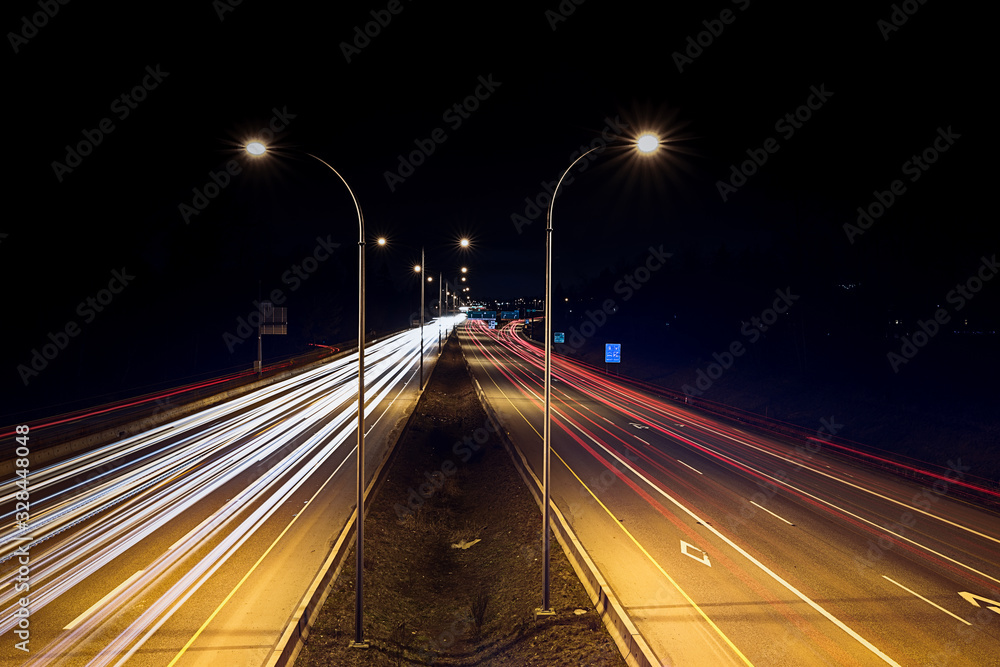 Speed traffic - light trails on highway at night. Cars exiting highway