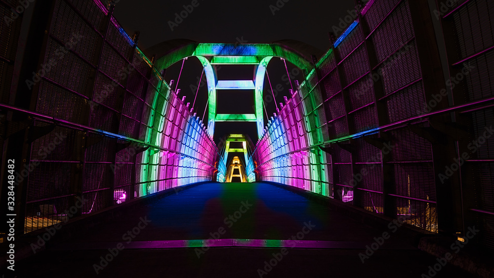 Bright colors illuminate pedestrian walkway over highway at night