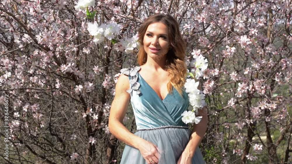 Model in a fancy dress posing with a blooming almond tree with a mountain valley in the background. Spring time nature awakening Model in a fancy dress posing with a blooming almond tree with a mountain valley in the background. Spring time nature awakening