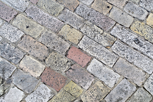 A fragment of an old cobblestone pavement lined with multi-colored rectangular bricks. Close-up. Background. Pattern.