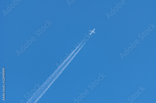 A distant bright white plane with a translucent conversion trail in a bright blue sky. Passenger airliner. Telephoto. Background. Travel concept.