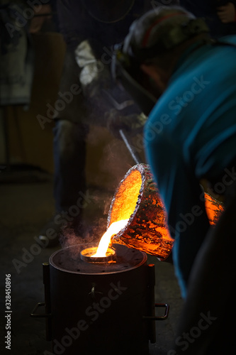 Molten bronze poured into mold by melter in foundry workshop