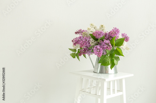 Bouquet of lilac in tin jug on stand indoor. With space for your text