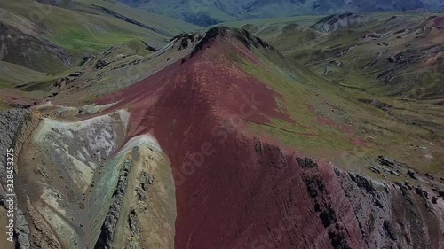 Aerial, tilt up, drone shot revealing a red peak and geological formations, snowy mountains in the background, in Valle Rojo Valley, Andes, Peru, South America photo