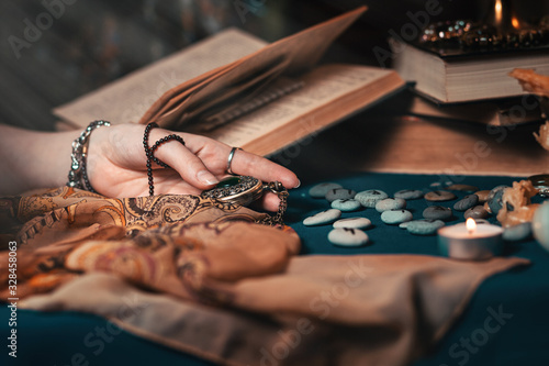 Astrology and esotericism. The female hand of the sorceress holds an amulet in her hands. In the background, old books, fortune-telling runes, and a candle. Copy space