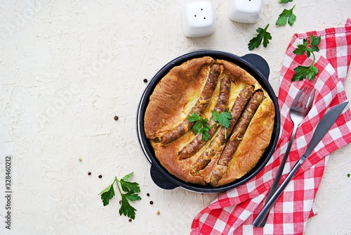 Pork sausages baked in pastry for Yorkshire pudding in a serving cast-iron skillet on a light concrete background. Toad in a hole recipe. British cuisine. Top view, copyspace photo