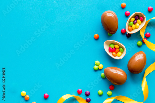 Easter background with chocolate eggs and dragees on blue background top-down frame copy space