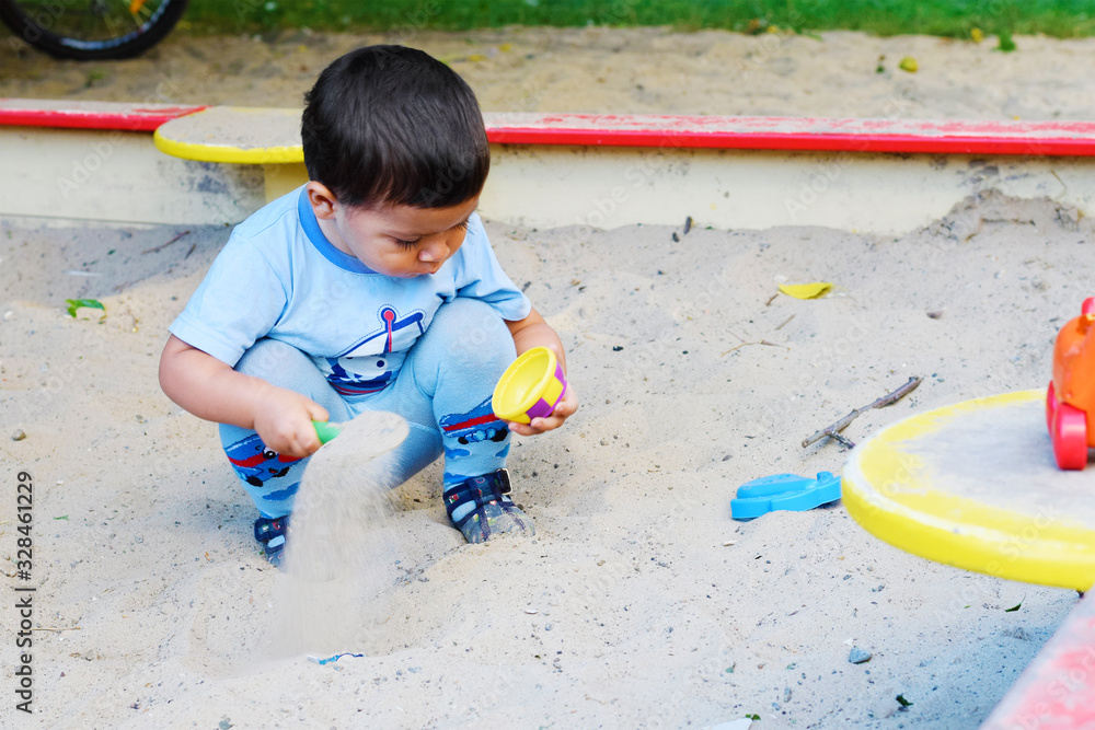 Fototapeta premium Little latin boy playing with sand in the sandbox.