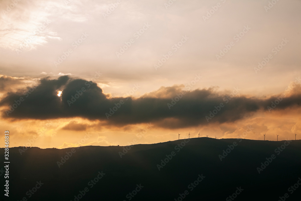Panoramic of a landscape with mountains at sunset with windmills, the sun and clouds
