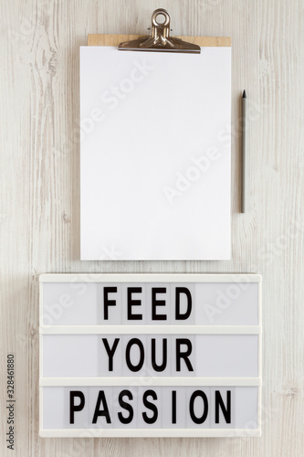 Fototapeta Naklejka Na Ścianę i Meble -  'Feed your passion' words on a lightbox, clipboard with blank sheet of paper on a white wooden background, top view. Overhead, from above, flat lay.