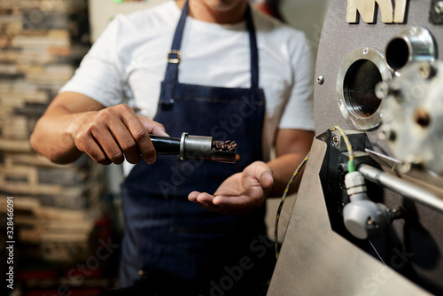 Cropped image of young man in apron showing probe of fresh roasted coffee beans