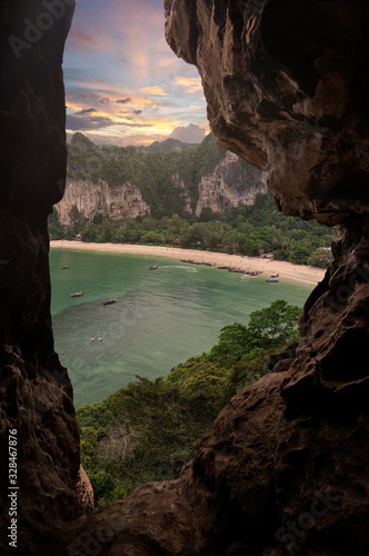 Railey beach view from cave on top of high cliff and longtail boat on tranquil sea in sunset sky © patiwat