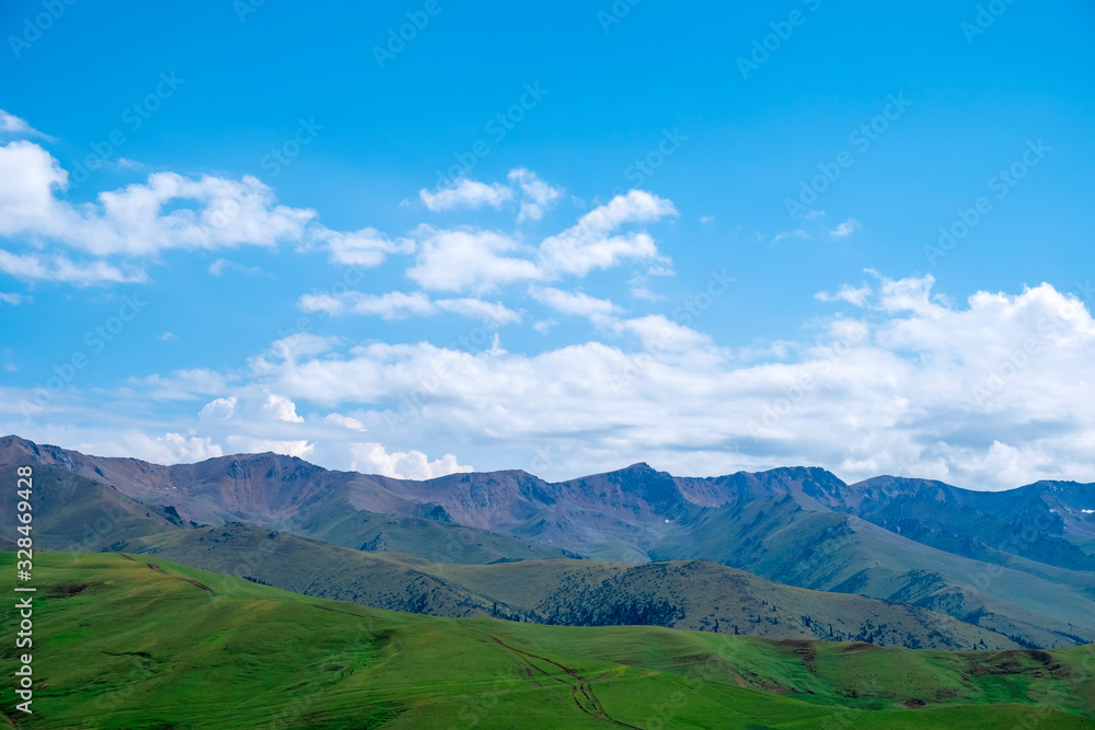 Beautiful green mountains on blue cloudy sky backdrop. Countryside landscape, nature. Natural scene. Beautiful view to Zaili-Alatau mountain range, captured from Assy plateau.