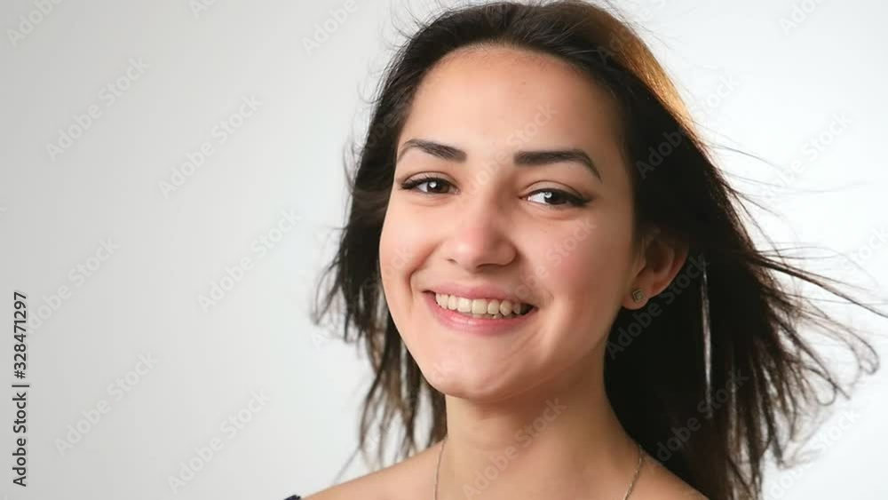 Happy brunette girl with waving long hair standing and smiling cheerily in a studio Happy brunette girl with waving long hair standing and smiling cheerily in a studio