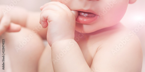 The child bites his finger his teeth are teething. Close- up of the baby's pen, mouth and teeth. Soft pink color. Baby teeth grow.
