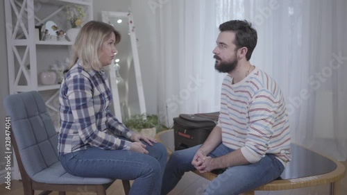 Nervous young woman yelling and hitting bearded husband with finger. Angry wife scolding husband indoors. Relationship problems, lifestyle, marriage, breakup, conflict, divorce.