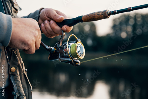 Fototapet Fishing rod with a spinning reel in the hands of a fisherman.