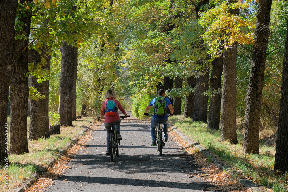 Young couple riding bicycles in autumn park.
