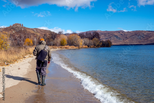 Fisherman with fiching rod on a lake in autumn. Man fisherman is catching a predator fish.