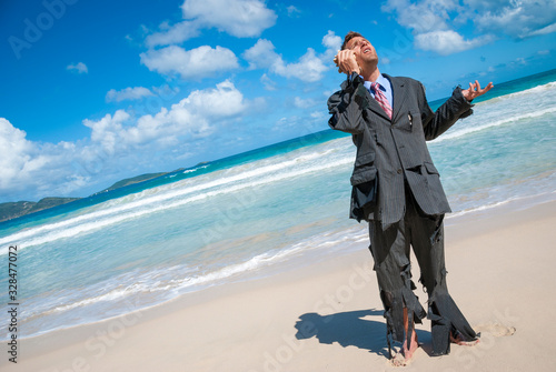 Stranded castaway businessman standing on the beach in his ragged suit, having an imaginary conversation on his shell phone