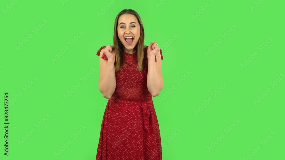 Tender girl in red dress is looking at the camera with excitement, then celebrating her victory. Green screen Tender girl in red dress is looking at the camera with excitement, then celebrating her victory. Green screen