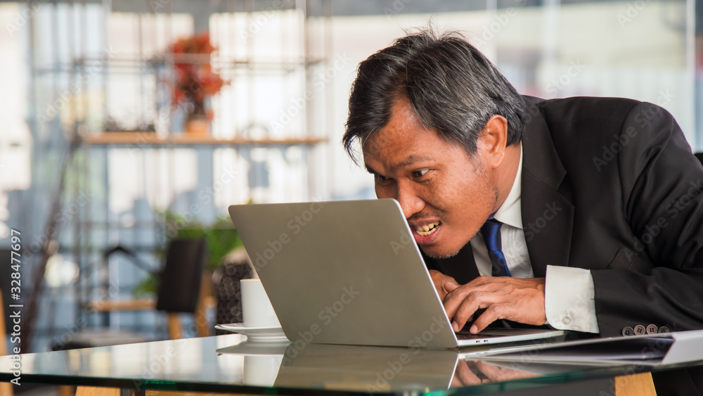 Fototapeta premium Close up crazy middle Asian businessman typing a laptop on table in coffee shop