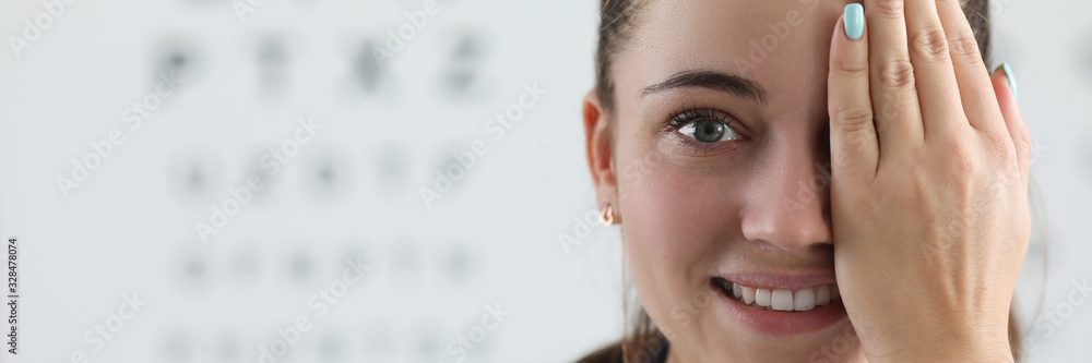 Portrait of lady oculist smiling and looking at camera with happiness. Cheerful doctor standing in clinic office and covering left eye with tender hand. Vision test concept - obrazy, fototapety, plakaty 