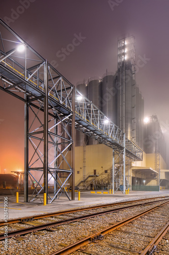 Foggy night scene with rails and pipeline overpass at petrochemical production plant, Port of Antwerp.