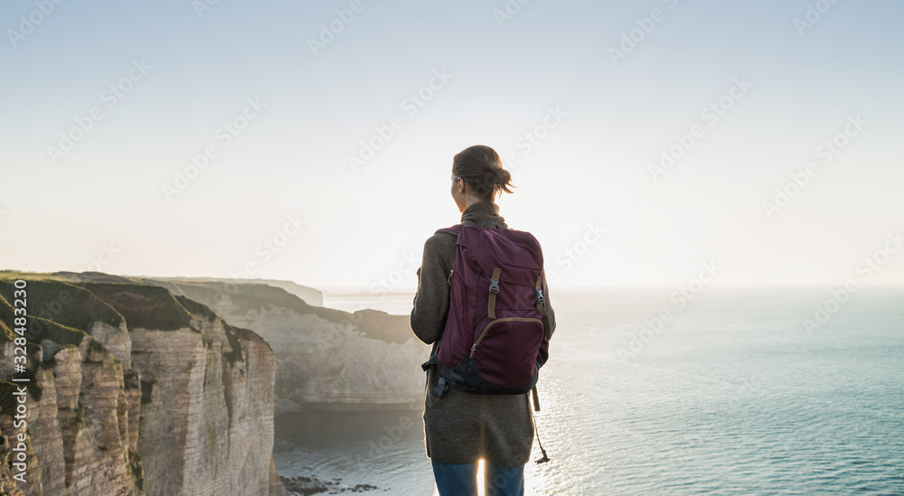 Young woman traveler with backpack looking at sea in Normandy, France over beautiful cliffs background, Travel, active lifestyle and summer holiday concept Young woman traveler with backpack looking at sea in Normandy, France over beautiful cliffs background, Travel, active lifestyle and summer holiday concept