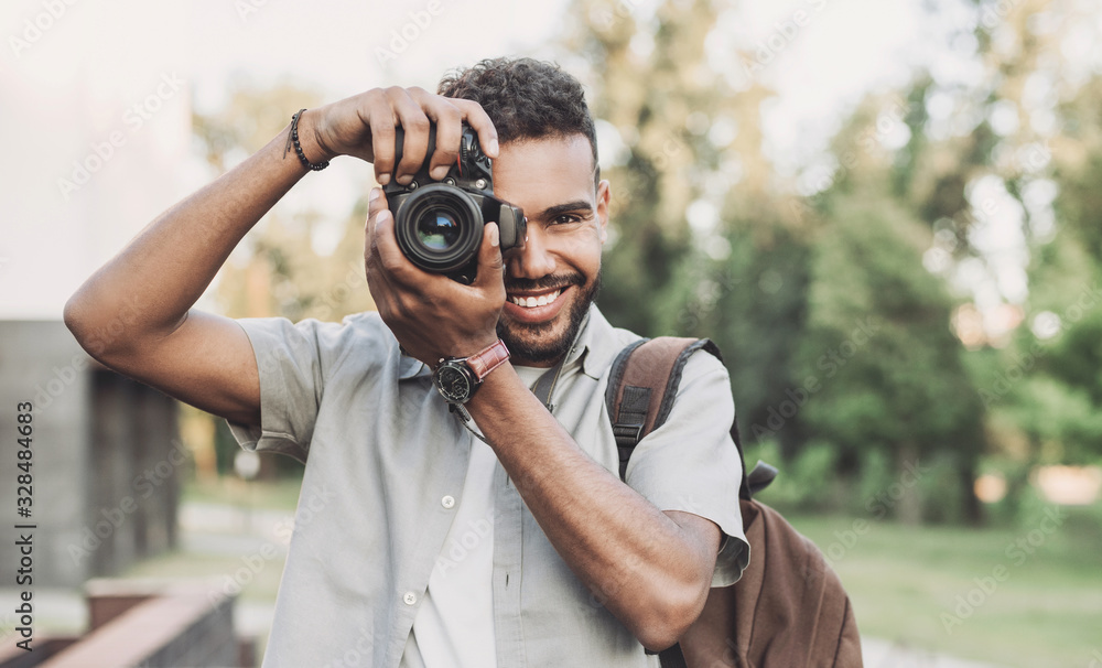 Young man photographer takes photographs with dslr camera in a city. Travel, vacations, professional freelance work and active lifestyle concept - obrazy, fototapety, plakaty 