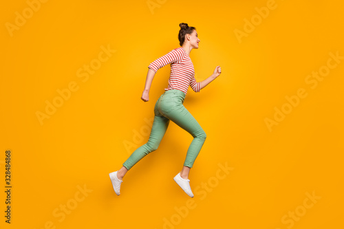 Full body profile photo of attractive pretty lady jumping high up rushing low prices shopping wear red white pullover shirt green pants footwear isolated bright yellow background