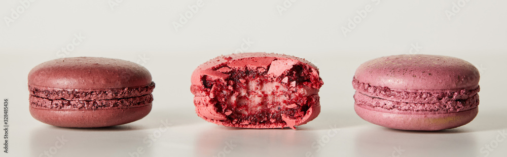 delicious whole and one bitten red french macaroons on white background, panoramic shot delicious whole and one bitten red french macaroons on white background, panoramic shot