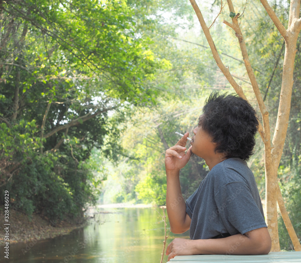 Asian handsome man is sitting and smoking in the forest. Asian handsome man is sitting and smoking in the forest.
