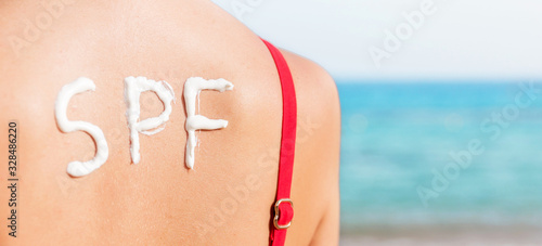 SPF word made of sunblock at woman's back at the beach. Sun protection factor concept photo