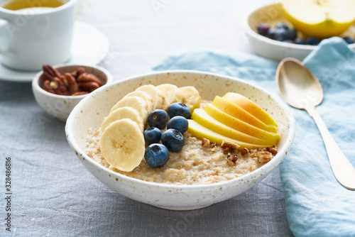 Whole oatmeal, large bowl of porridge with banana, blueberries, apple, nuts. Side view, close up